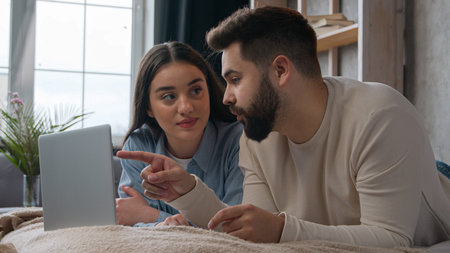 Relaxed couple family lying on bed use computer laptop online shopping together make order internet...