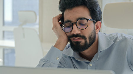 Tired lazy Indian man Arabian businessman manager bored yawn at office desk boring computer work...
