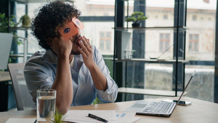 Funny lazy worker napping at office tired business man sleeping covering eyes with sticky notes comical stickers on face employee businessman yawning pretend working to sleepの写真素材