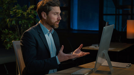 Busy Caucasian man businessman sit at evening office chatting in video conference talking indoors...