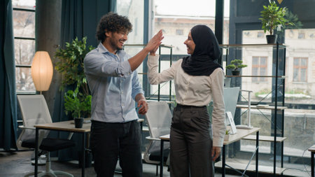 Two multiracial colleagues happy company coworkers Arabian Indian man businessman giving high five muslim woman businesswoman in hijab business people smiling together teamwork partnership in officeの写真素材