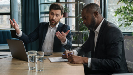 Caucasian manager showing African boss bad business result computer mistake two diverse men multiracial coworkers businessmen with papers and laptop sad upset failure discuss startup problem at officeの写真素材
