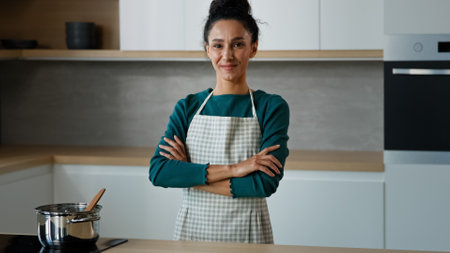 Beautiful arabian cooker chef baker housewife ethnic young vegetarian woman posing in modern kitchen female portrait of satisfied spanish lady mother prepare meal for family standing with crossed armsの写真素材