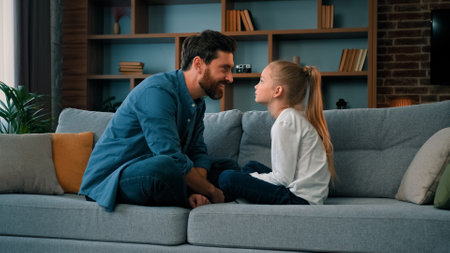 Playful caucasian young family daddy and small daughter sitting comfortable on couch loving cute girl touching father nose funny joke playing game with parent having fun spending free time togetherの写真素材