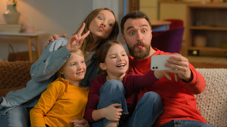 Caucasian happy family mother father kids little girls daughters posing grimace photo on mobile phone at evening home funny parents children record video online blog smartphone selfie social media appの写真素材
