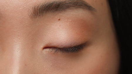 Extreme close up female dark eyes details Asian woman girl ethnic healthy lady eyesight human eye opening iris eyeball blink eyelash gaze vision beauty face skincare cosmeticsの写真素材