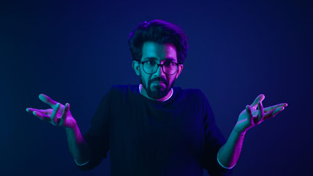 Studio dark blue neon background Indian man Arabian male model guy confused shrug shoulders unsure...