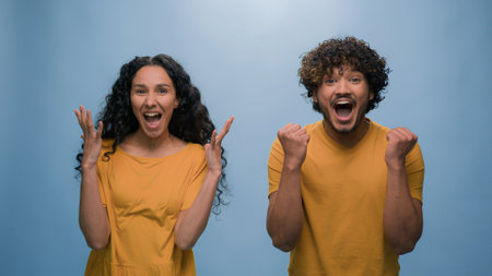 Excited happy shocked wonder amazed surprised couple winners man woman amazing good news achieve win victory achievement triumph shout screaming yelling winning blue studio backgroundの写真素材