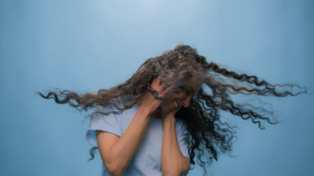 Active happy girl dancing woman female cheerful model in headphones listening music dance fun moving enjoy free movement flying curly hair listen song at blue studio backgroundの写真素材