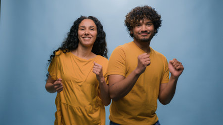 Multiracial diverse couple Indian Arabian man guy Hispanic Caucasian woman girl dancing together to music having fun enjoying funny active moving dance fooling around entertainment at blue backgroundの写真素材