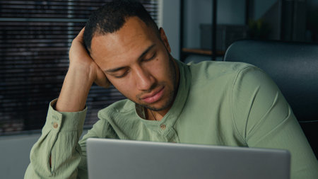 Tired lazy young african american businessman bored at work fall asleep at office desk sleepy overworked ethnic man employee sleeping at workplace near laptop napping resting feel exhaustion fatigueの写真素材