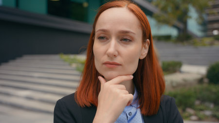 Portrait pensive thinking serious Caucasian ginger hair business woman in city outdoors businesswoman think problem solution idea pondering brainstorm thoughtful rubbing chin girl difficulty questionの写真素材