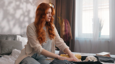 Caucasian woman girl female lady traveler prepare travel vacation trip journey preparation put clothes in suitcase luggage baggage at home bedroom on bed relocation moving day traveling anticipationの写真素材