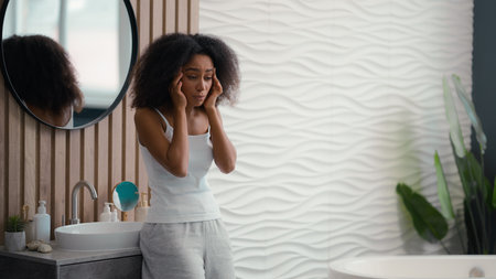 African American sad upset sick girl biracial ethnic lady woman in bath bathroom feel bad discomfort head pain headache painful ache symptom health problem need painkiller migraine hangover pressureの写真素材