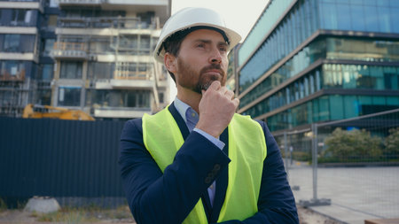 Caucasian pensive adult man heavy metal building industry worker inspector thinking architect looking at skyscrapers contractor think engineer in hardhat thoughtful dissatisfied frustrated problemの写真素材
