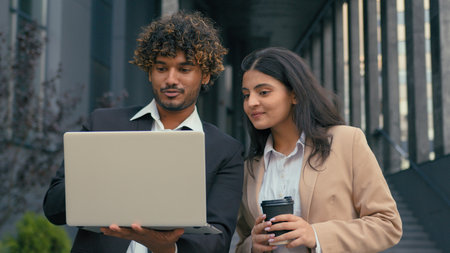 Indian Arabian trader estate agent salesman businesswoman consulting client customer woman businesswoman in city near office building skyscrapers business partners with laptop computer talk outdoorsの写真素材