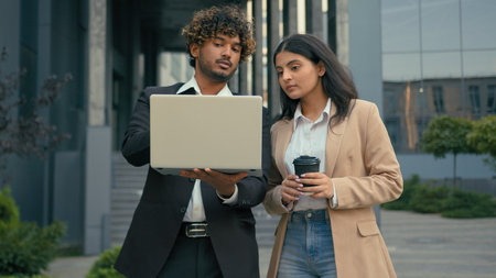 Two business colleagues talking pointing at laptop in city outdoors Arabian employees woman cooperating startup project work brainstorming looking at computer discussing Indian man strategy discussの写真素材