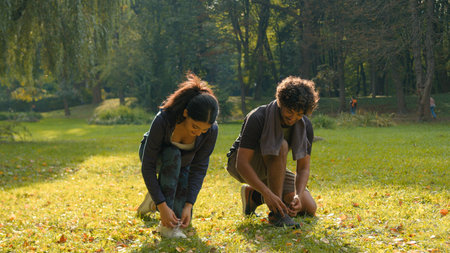 Two people woman man runners sportive girl guy Indian Arabian couple standing in park outdoors forest talking friendly speaking talk tying sneakers tie shoelaces of shoes together prepare to sportの写真素材