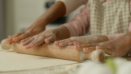 Close up cropped view hands arms African woman mother female mom teaching little child kid girl daughter cooking pastry pizza baking teach using rolling pin together at kitchen table dough cook pieの写真素材