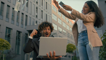 Two business people in city Indian happy rejoice yelling happy winner businessman worker man celebrate online win laptop winning lottery financial growth Arabian businesswoman woman throw money rainの写真素材