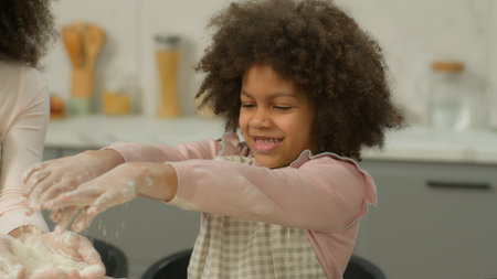 African American family cooking together mother woman mom teach little child kid girl daughter help mommy funny fun fooling play with white wheat flour cook dough at kitchen food delivery baking smileの写真素材
