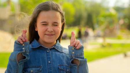 Caucasian child little girl schoolgirl crossing fingers hope adopted kid female orphan wish happy family adoption children believe in miracle pray ask god bless in city outdoors aspirations dream luckの写真素材