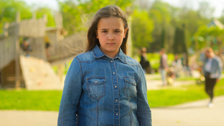 Portrait in park city outdoors offended angry alone sad serious Caucasian girl little child kid daughter adopted family bad mood frowning schoolgirl pupil posing crossed hands offenseの写真素材