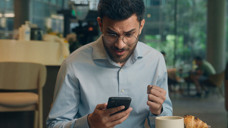 Arabian man ethnic muslim Indian businessman guy entrepreneur manager using mobile phone business lunch in cafe restaurant male visitor millennial tourist read message cellphone expect smartphone smsの写真素材