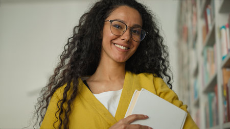 Happy Arabian Latina Hispanic woman student library university bookstore reader reading favorite book study smile hobby female girl learning literature bookworm high school education textbook collegeの写真素材
