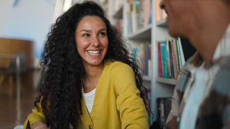 Indian Arabian Latina woman African American man classmates friends students talking laughing together two people communicate library university high school college learning girl guy smiling educationの写真素材
