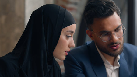 Two multiracial colleagues Arabian man muslim woman in hijab girl guy coworkers business partners businesswoman businessman male boss mentor help female intern teach employee office online data laptopの写真素材