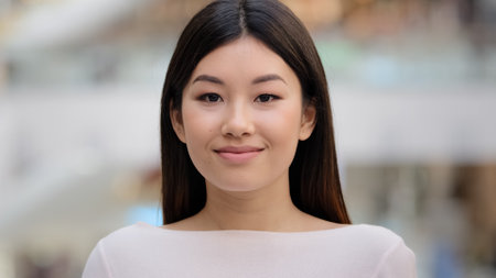 Close up female indoors headshot Asian happy smiling millennial girl. 20s brunette woman model lady with natural make-up face cosmetology service. Businesswoman worker manager client looking at cameraの写真素材