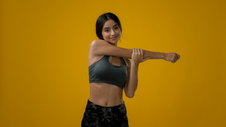 Strong slim Indian woman sporty girl sports lady sport female athlete model in yellow studio background workout exercise stretching hands head bending neck body care yoga fitness stretchの写真素材