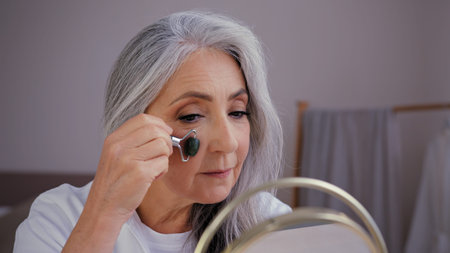 Close-up old gray-haired Caucasian woman model grandma elderly lady looking in mirror smooth out...