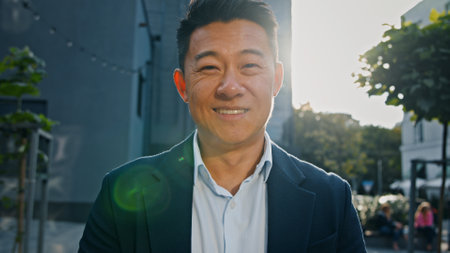 Front view portrait smiling happy Asian middle-aged businessman Korean adult entrepreneur employer man worker manager investor architect standing in city outdoors posing in sun lights sunbeams sunsetの写真素材