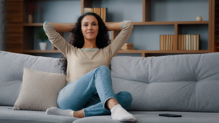 Calm happy in good mood caucasian hispanic latino 30s woman resting on couch new sofa in living room stretching hands behind head healthy lady relaxing in comfortable apartment real estate own homeの写真素材