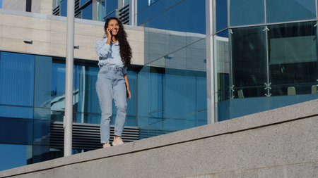 Young cheerful beautiful brunette business woman winner carefree girl walking on urban blue glass...