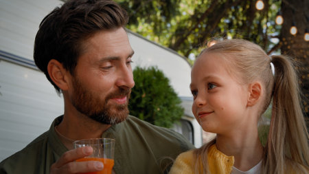 Close up Caucasian adult father bearded dad with little daughter child schoolgirl kid drinking fresh orange juice outdoors at camping picnic dinner refreshment talking together enjoy healthy drinkの写真素材