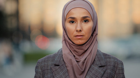 Close up portrait sad upset female face pensive serious muslim business woman young islamic girl ethnic lady wearing hijab stands in city looks away looking at camera religious discrimination conceptの写真素材