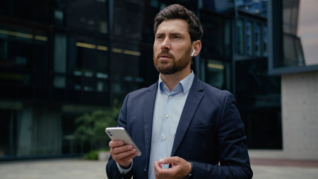 Caucasian man businessman adult entrepreneur guy male business consultant employer in wireless earphones answer mobile phone call outside talk cellphone smartphone call using gadgets in city outdoorsの写真素材