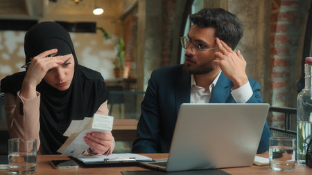 Business colleagues Arabian man muslim woman in hijab bank payment laptop count bills check invoice financial problem account debt bankruptcy upset frustrated stressed businesswoman businessman officeの写真素材