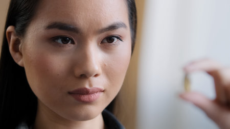 Extreme close-up female blurred female face asian girl korean sick ill woman holding vitamin pill holds medicine capsule against minerals food supplement. Healthy quality life health care conceptの写真素材