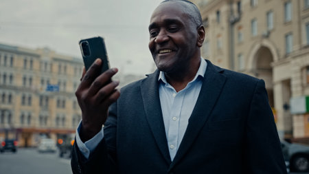 African middle-aged adult ethnic male man consultant employer businessman entrepreneur in city street outdoors talking mobile phone camera talk speaking smartphone video call conference virtual chatの写真素材