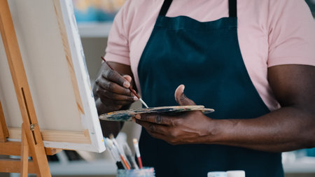 Close-up of male hands unrecognizable African man artist painter holding palette with bright oil acrylic paints colors drawing creates picture on canvas and easel using painting with brushes drawの写真素材