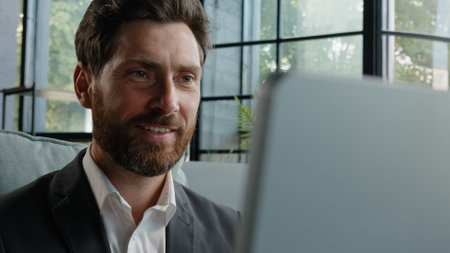 Happy dreaming smiling Caucasian bearded adult 40s man work with computer online write article looking away dreaming thinking pondering business strategy plan smile satisfied typing laptop in officeの写真素材