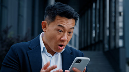 Happy shocked amazed 50s years man in formal suit standing outdoors looking phone in city 40s winner businessman has business success amazing news offer wonder with smartphone winning with mobile winの写真素材