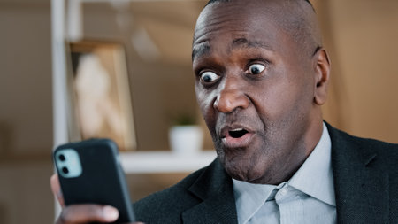 African American old 50s surprised amazed shocked man looking at mobile phone screen reading unbelievable news waving head no disagreement negation refusal shock fear amazing online sms shock reactionの写真素材