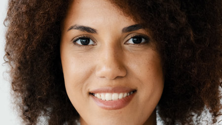 Front view female smiling toothy perfect dark skin natural make-up face. Close up African American curly woman girlfriend biracial lady look at camera open and confident smile with healthy white teethの写真素材