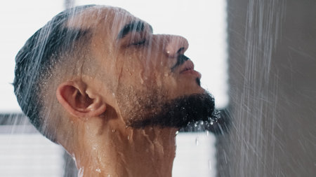 Arab bearded man in shower washing head showering in bathroom at home close up. Millennial brunette guy rinsing shampoo and conditioner from hair in warm bath hot water runs down faceの写真素材