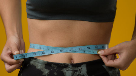 Close up female abdominal body part tummy cropped view unrecognizable sport woman with measuring tape measure waist unknown sporty slim lady girl fitness weight loss calories checking torso progressの写真素材